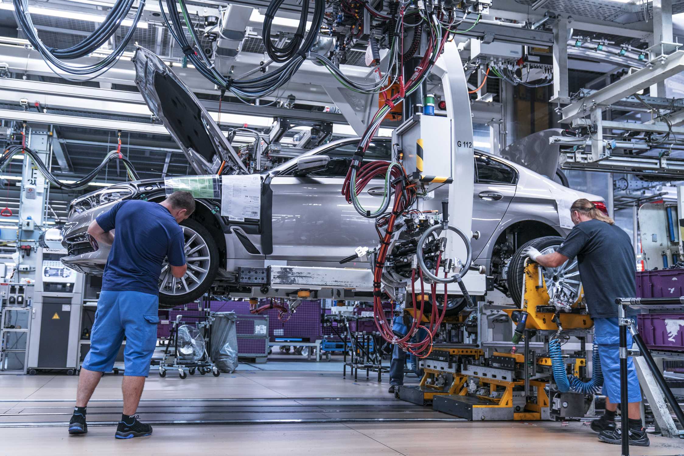 Workers fitting wheels to a car on an automotive assembly line